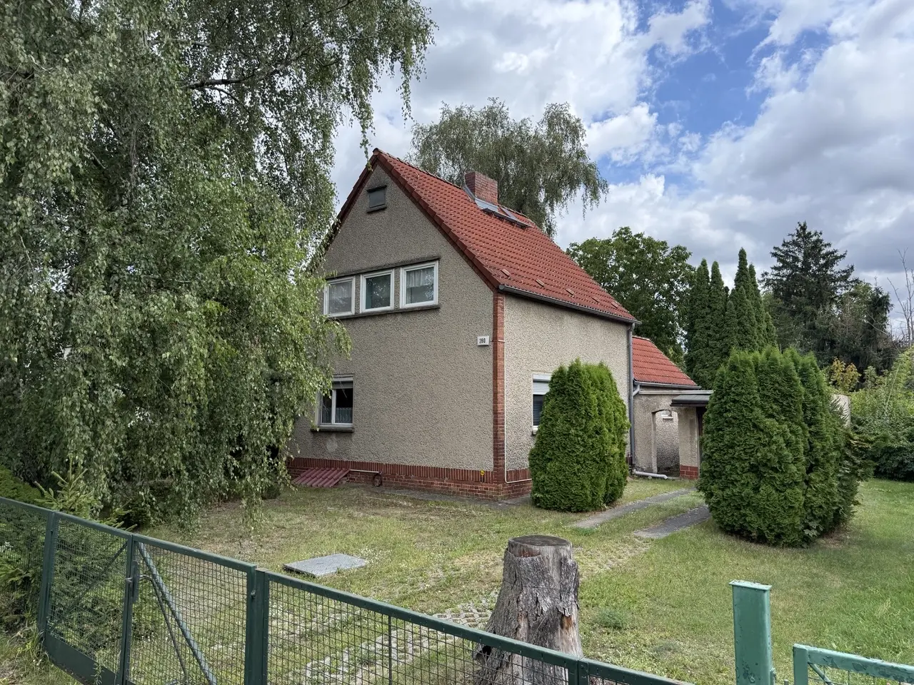 Siedlungshaus Hönower Straße 280 in Mahlsdorf mit rotem Ziegeldach und sichtbarer roter Ziegelecke, umgeben von einem großen Garten mit Baumstumpf